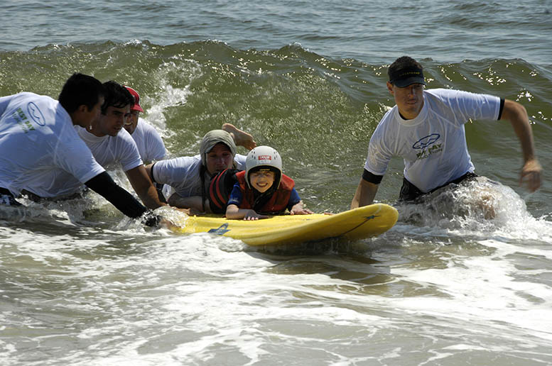 Special Needs Child on a surfboard in the water with adults