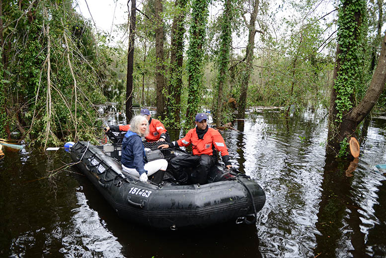 Coast Guardsmen and Civilian woman riding on a floating raft during a flood.