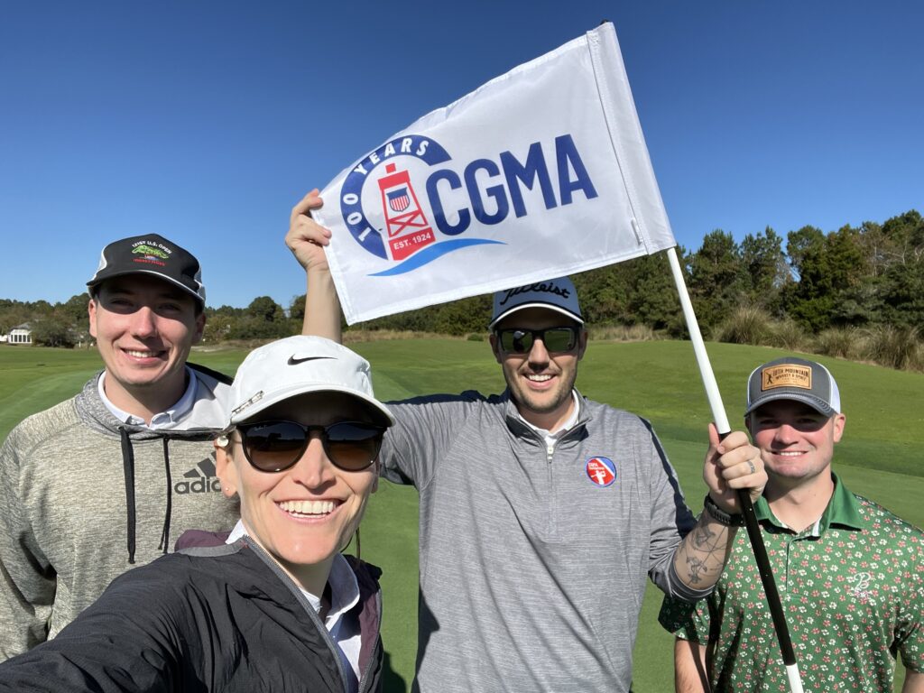 CGMA Open golfers smile on a golf course while holding a CGMA 100 Years flag.